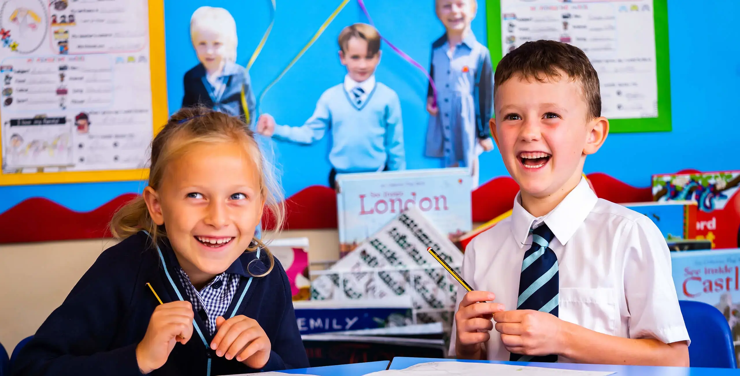 Two King’s Ely Pre-Prep students sitting at a desk, smiling and looking to camera. 